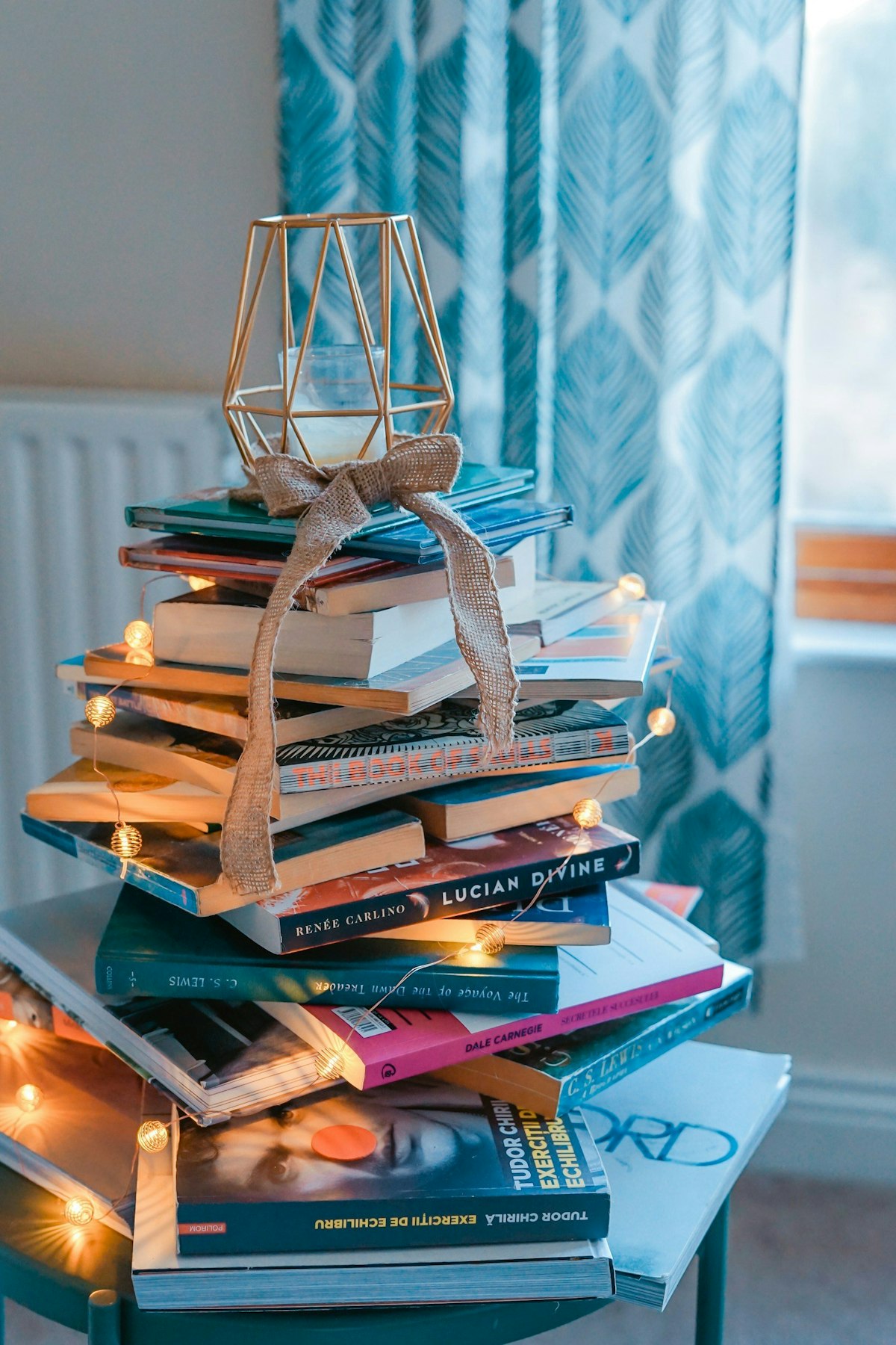 A stacked of books wrapped in twinkly lights with a candle holder rested atop