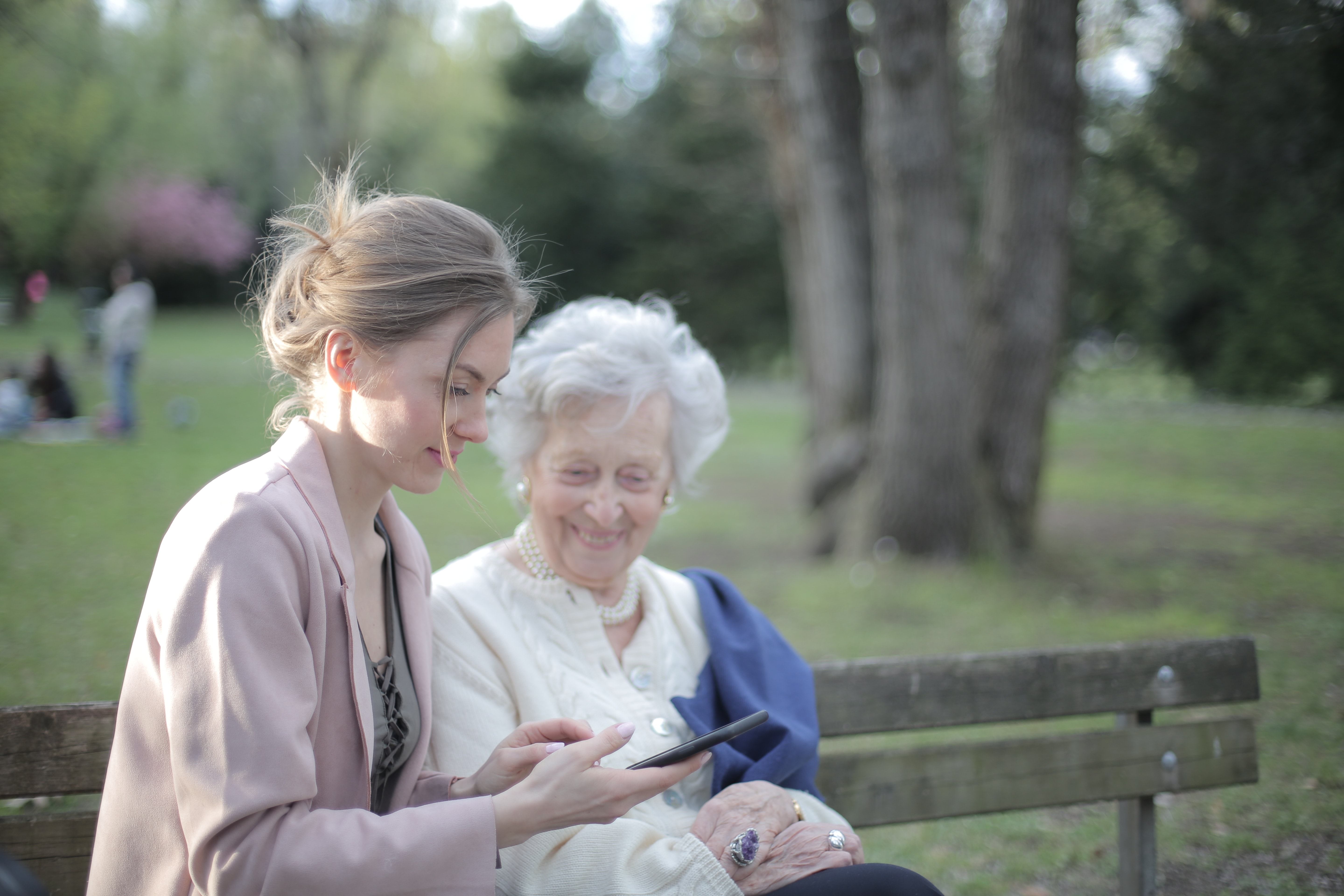 Caregiver in park with elderly patient showing her how to use smartphone.