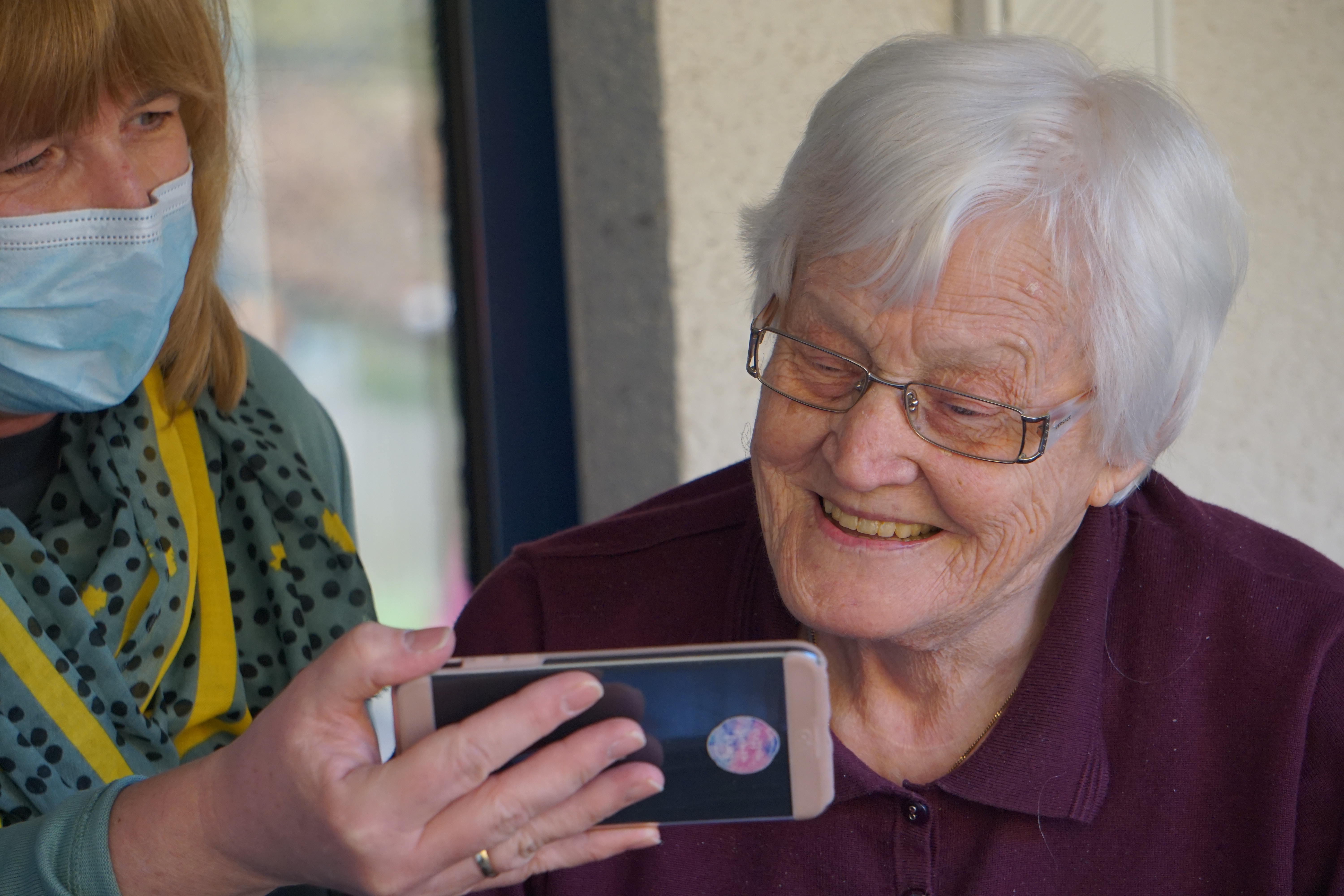 Caregiver showing elderly patient video on smartphone.