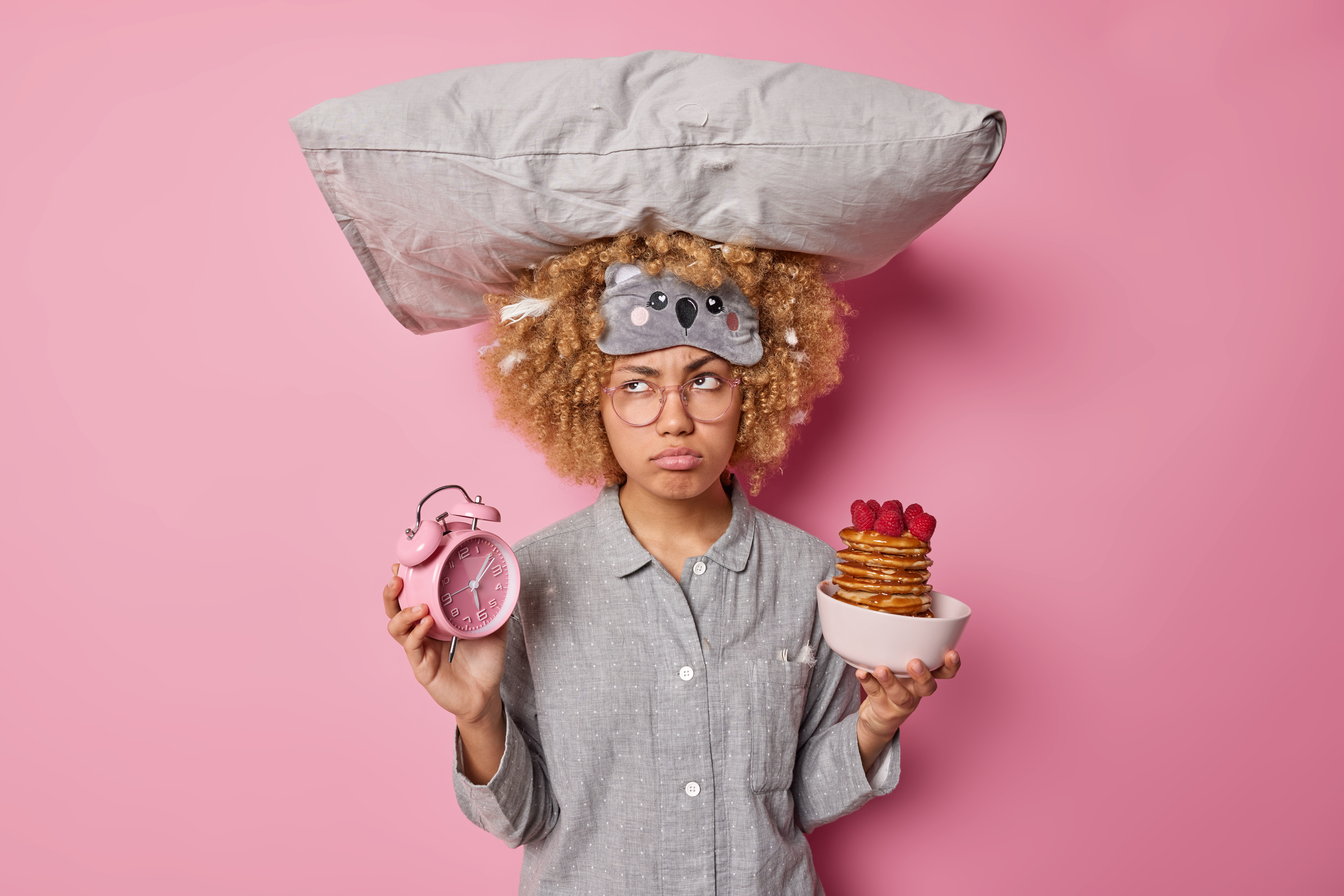 upset-young-woman-dressed-pajama-carries-pillow-head-holds-alarm-clock-bowl-pancakes-with-raspberries-has-sad-pensive-expression-isolated-pink-background-morning-time-concept.jpg