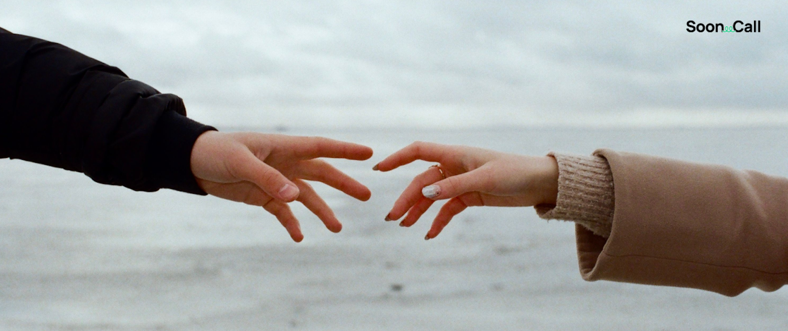A close-up of two hands reaching towards each other against a calm sea backdrop, evoking connection and emotion
