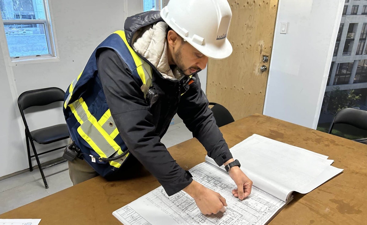 Construction site leader reviewing blueprints in site office wearing Lanterra hard hat and safety vest