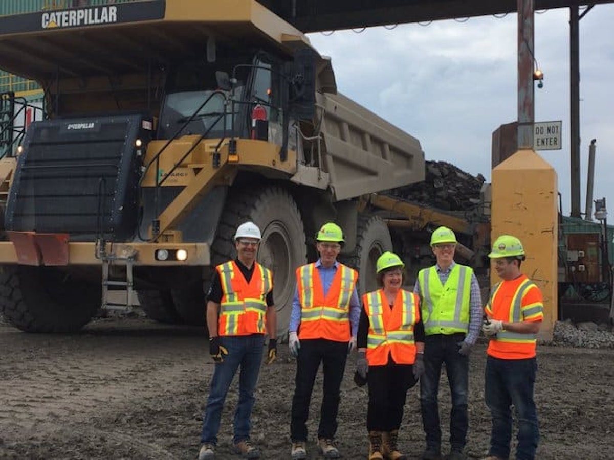 A group of Lafarge Dundas Quarry employees wearing hard hats and high-visibility safety vests stand together in front of a large Caterpillar haul truck at the quarry. The image represents skilled hourly workers, industrial operations, and teamwork in aggregate mining and materials production.