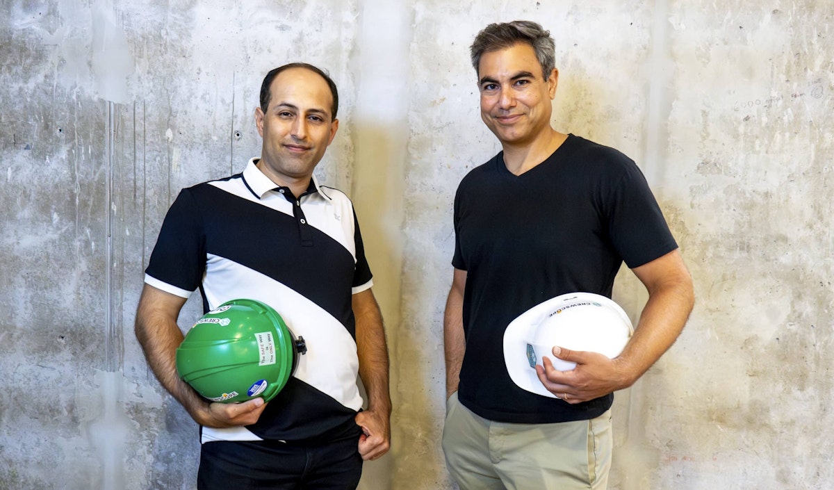Crewscope co-founders Ehsan Foroughi (CTO) and Calvin Benchimol (CEO) holding branded hard hats against concrete wall