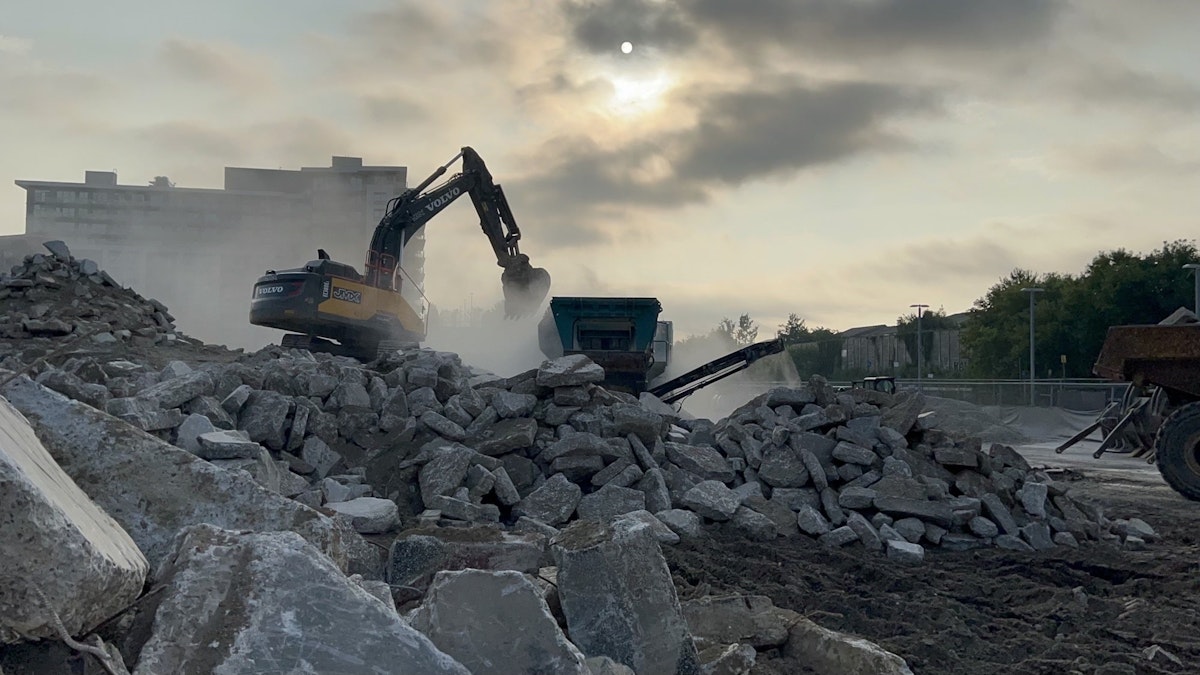 Excavator loading broken concrete into a crusher at an active construction site during early morning light.