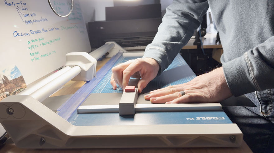 video editor uses paper cutter to create backing for wall card printed as a collage from moments contained in client video