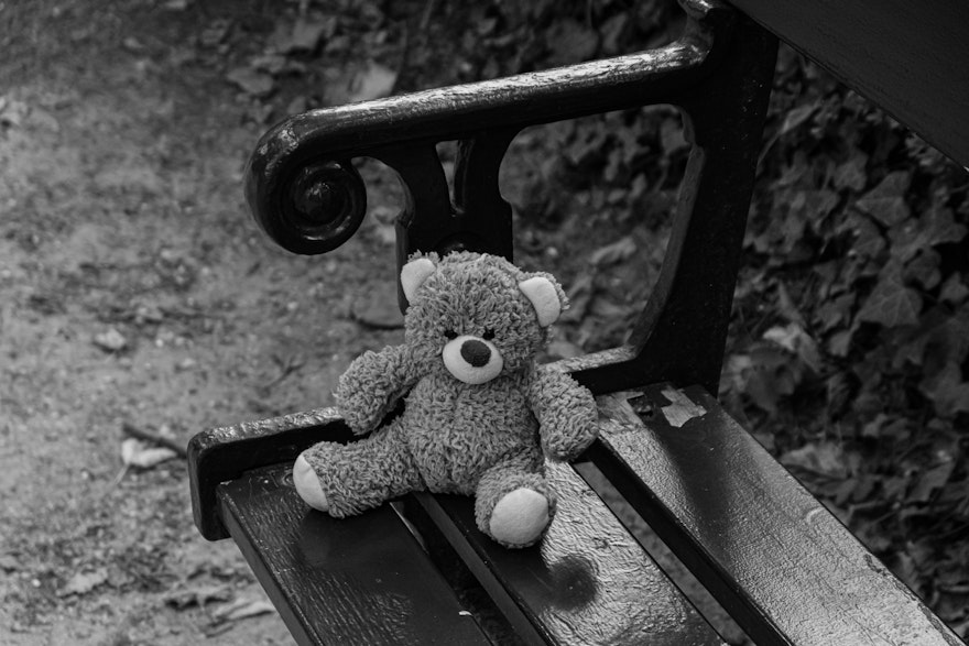 Black and white image of a teddy bear on a bench