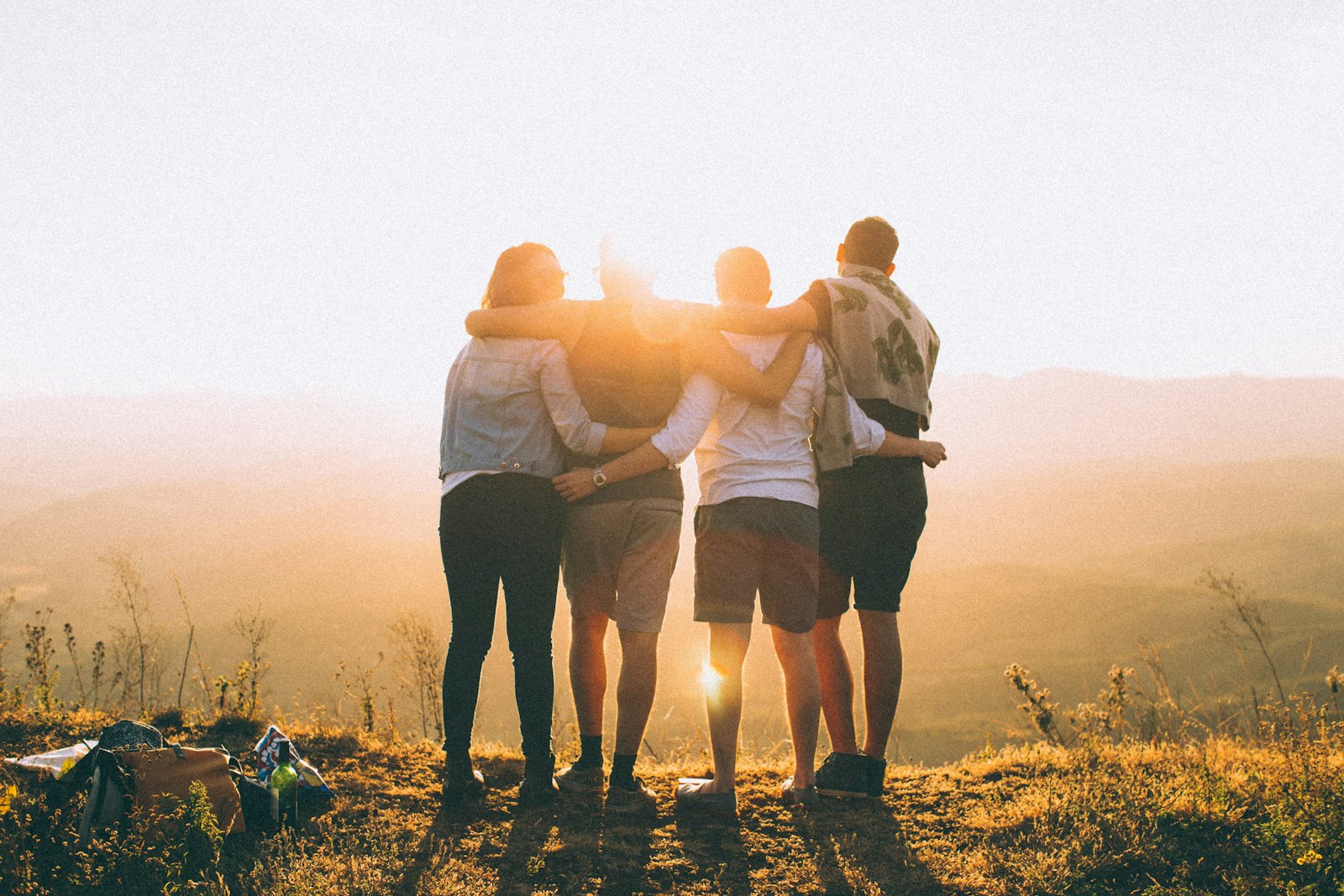 Fyra personer står och tittar mot soluppgången och håller om varandra. 